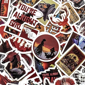 May include: A collection of Western-themed stickers with various designs and text. Stickers include images of cowboys, horses, and the text "YOU'RE ALRIGHT GIRL" and "RED DEAD REDEMPTION II". The color palette includes red, brown, and white.