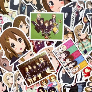 Pode incluir: Uma cole&ccedil;&atilde;o de autocolantes em estilo anime com v&aacute;rios personagens e cenas. Os autocolantes mostram v&aacute;rias poses e express&otilde;es, com foco em um grupo de meninas tocando instrumentos musicais. A paleta de cores inclui marrons, verdes e rosas.