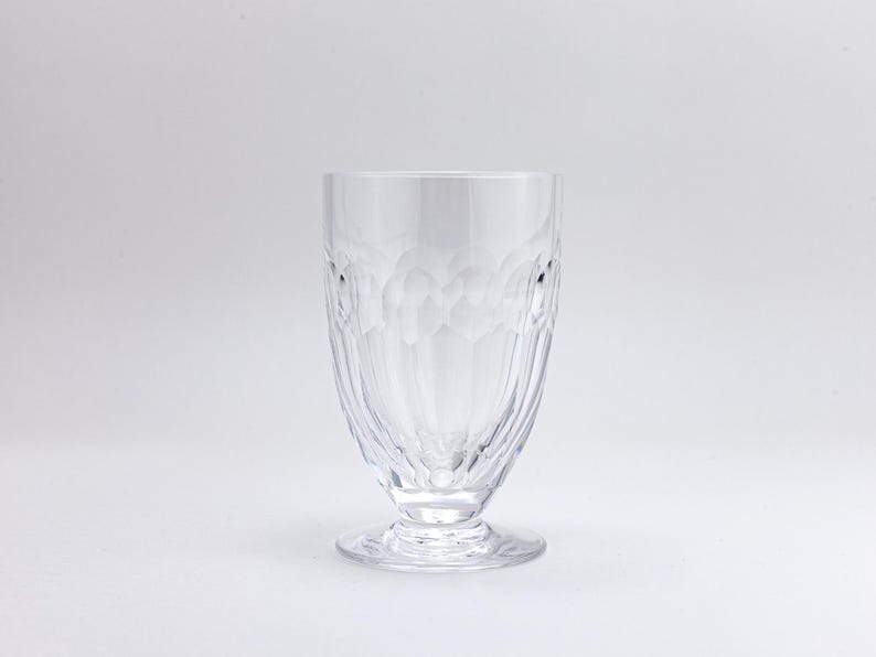 Op de afbeelding: Een helder drinkglas met steel en een gestructureerd patroon. Het glas heeft een brede, afgeronde body die taps toeloopt naar een kleinere voet. Het glas is gemaakt van helder glas en staat tegen een witte achtergrond.