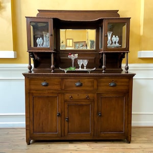 Op de afbeelding: Een antiek buffet van donker hout met een spiegelrug en glazen deuren. Het buffet heeft drie lades en drie kastdeuren.