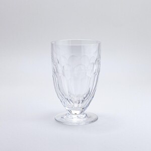 Op de afbeelding: Helder glas met voet en een gestructureerd patroon. Het glas heeft een afgeronde komvorm en een kleine, cirkelvormige voet. Het glas is gemaakt van helder materiaal en is geschikt voor het serveren van dranken.