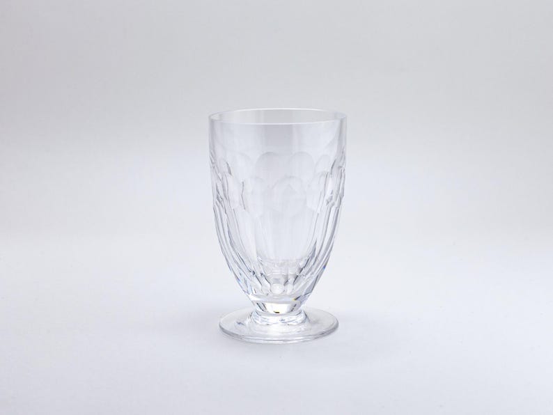 Op de afbeelding: Helder glas met voet en een gestructureerd patroon. Het glas heeft een afgeronde komvorm en een kleine, cirkelvormige voet. Het glas is gemaakt van helder materiaal en is geschikt voor het serveren van dranken.