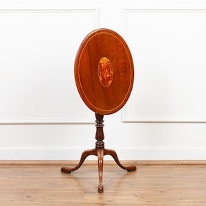 May include: A vintage, oval-top side table. The table features a dark brown wooden surface with a lighter-colored oval inlay. It stands on a pedestal base with three curved legs. The table is approximately 28 inches tall.