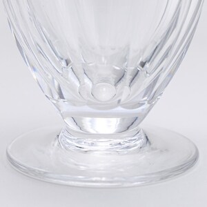 Op de afbeelding: Close-up van een helder glas met voet en een brede, cirkelvormige basis. Het glas heeft een uitlopende kom met verticale, getextureerde lijnen. De basis is een platte, cirkelvormige schijf. Het glas is transparant.