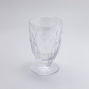 Op de afbeelding: Een helder drinkglas met een textuurpatroon, staand op een kleine voet. Het glas heeft een brede opening en een patroon op de body. Het glas is leeg en lijkt van kristal of een vergelijkbaar materiaal te zijn. De hoogte is ongeveer 15 cm.