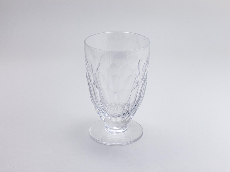 Op de afbeelding: Een helder drinkglas met een textuurpatroon, staand op een kleine voet. Het glas heeft een brede opening en een patroon op de body. Het glas is leeg en lijkt van kristal of een vergelijkbaar materiaal te zijn. De hoogte is ongeveer 15 cm.