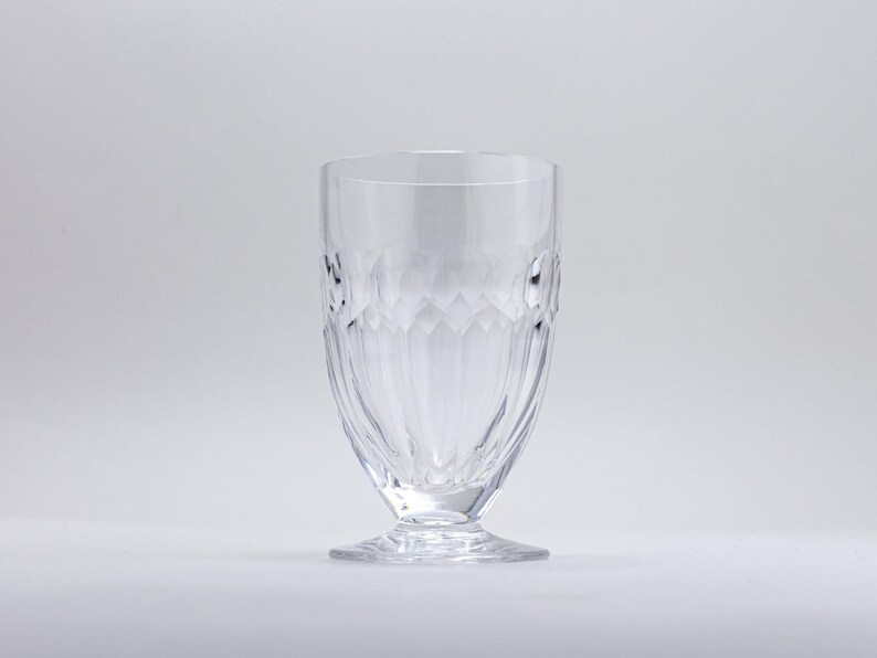 Op de afbeelding: Een helder drinkglas met voet en een gestructureerd, diamantachtig patroon aan de zijkanten. Het glas heeft een brede, stabiele basis en een gladde rand. Het ontwerp is symmetrisch en elegant, geschikt voor het serveren van dranken.