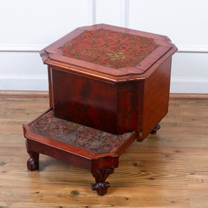 May include: A wooden step stool with a red and gold patterned top. The stool has a small storage compartment and four carved legs.