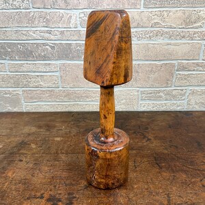 May include: A wooden mallet with a rounded head and a cylindrical handle. The mallet is made of dark brown wood with a natural finish.