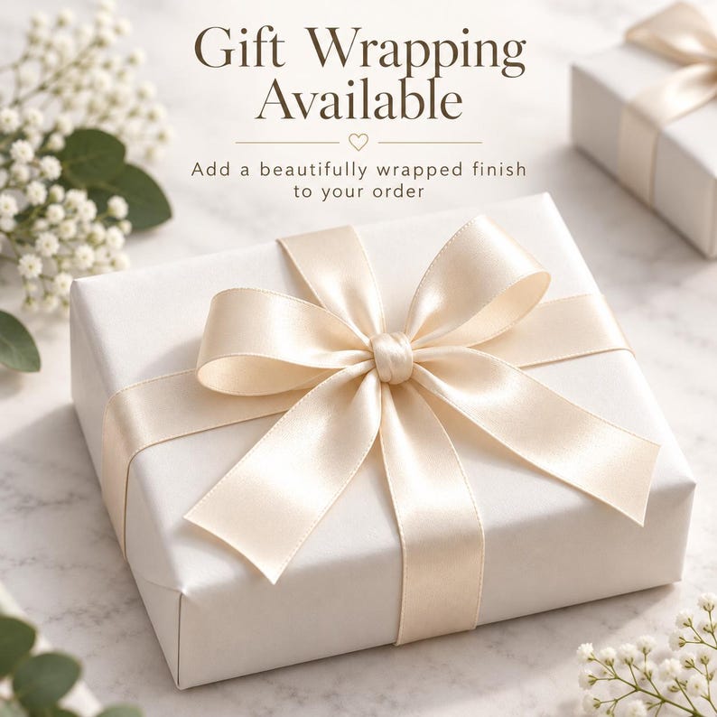 May include: A square gift box wrapped in plain white paper with a large, centered cream-colored satin ribbon bow. The text reads Gift Wrapping Available and Add a beautifully wrapped finish to your order with a small heart icon.