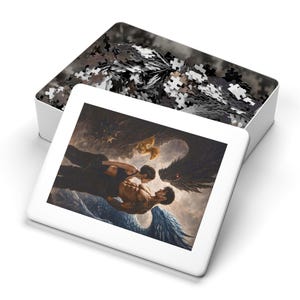 May include: A white puzzle box with a partially assembled puzzle inside. The puzzle lid features a dramatic image of two figures embracing, with angel wings and a dark, winged creature. The puzzle pieces are black, white, and gray.