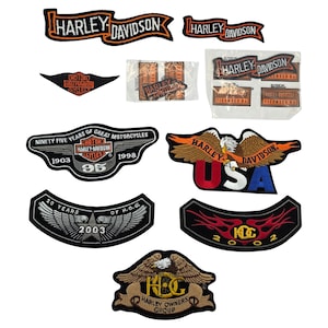Può includere: Una collezione di toppe Harley-Davidson in varie forme e design. Le toppe presentano il logo Harley-Davidson, aquile e testo come "USA", "20 Years of H.O.G." e "Ninety Five Years of Great Motorcycles".