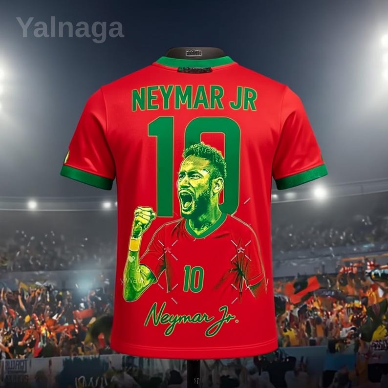 May include: Red soccer jersey featuring a green and white design, with the name "NEYMAR JR" and the number "10" in green. The jersey has a large graphic of Neymar Jr. celebrating. The jersey has green trim on the sleeves and collar.
