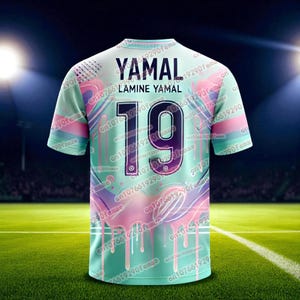 May include: A mint green soccer jersey with the name "YAMAL" and the number "19" on the back. The jersey has a colorful design with pink and purple accents. The jersey is displayed on a green field.