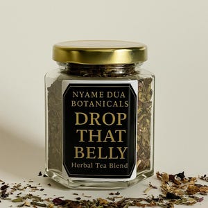 May include: A clear glass jar with a gold lid, filled with herbal tea blend. The label reads "NYAME DUA BOTANICALS DROP THAT BELLY Herbal Tea Blend." Loose tea leaves are scattered around the jar.