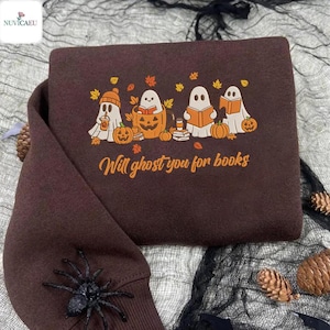 Könnte beinhalten: Ein dunkelbraunes Sweatshirt mit einem Halloween-Motiv. Das Design zeigt vier Cartoon-Geister mit Kürbissen, Büchern und Herbstblättern. Der Text "Will ghost you for books" ist in Orange gedruckt.