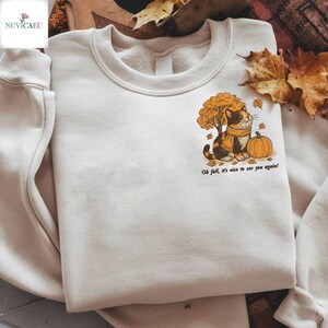 May include: Cream-coloured sweatshirt with a graphic of a cat wearing a scarf, sitting beside a pumpkin and a tree with autumn leaves. The text "Oh fall, it's nice to see you again!" is printed below the graphic.