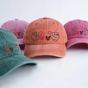 Könnte beinhalten: Eine Auswahl an Baseballkappen in verschiedenen Farben, darunter Grün, Rosa und Orange. Jede Kappe zeigt ein gesticktes Design mit dem Wort "love" und Mickey Mouse-Elementen. Die Kappen haben einen Vintage-Look.