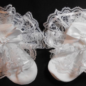 May include: A pair of white baby socks with lace ruffles and satin bows. The socks are made of soft cotton and are perfect for special occasions.