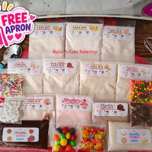 May include: A collection of Build-A-Cake Bakeshop cake mix pouches, icing packets, and various colorful candy toppings. The set includes a metal whisk, a blue-handled scoop, and a graphic featuring a pink apron with the text FREE APRON.