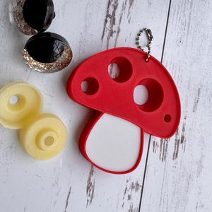 May include: A red mushroom-shaped keychain with three circular cutouts and a white base. Two black and gold glitter resin cabochons and two yellow resin wheels are also present.