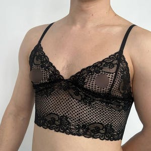 Puede incluir: Bralette de encaje negro con tirantes finos. El bralette presenta un diseño de encaje floral y una silueta larga. La prenda tiene un patrón delicado e intrincado y está diseñada para ser usada como lencería o top.