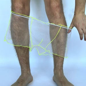 May include: Sheer white mesh boxer briefs featuring neon yellow piping along the seams and a white elastic waistband. The lightweight, translucent fabric is constructed with visible neon yellow stitching that outlines the leg openings and centre.