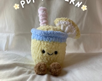 Könnte beinhalten: Ein handgefertigtes, gehäkeltes, gelbes Getränk mit blauem Band, rosa Strohhalm und braunen Pompon-Füßen. Der Text "PDF PATTERN" ist über dem Getränk angeordnet. Das Getränk hat ein lächelndes Gesicht und weiße und gelbe Akzente. Dies ist ein Häkelmuster.