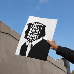 Puede incluir: Un cartel en blanco y negro se sostiene contra un cielo azul. El cartel presenta una silueta de la cabeza y los hombros de una persona con las palabras "FASCIST RACIST RAPIST" en texto blanco.