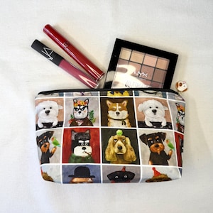 May include: A rectangular cosmetic bag with a zipper, featuring a repeating pattern of illustrated dogs in various outfits. The bag contains two lipsticks, a lip gloss, and a black eyeshadow palette.