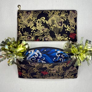 May include: Two black zippered pouches with gold koi fish and wave patterns. One pouch is open, revealing a blue and white wave pattern. The pouches have gold zipper pulls and are decorated with gold foil accents.
