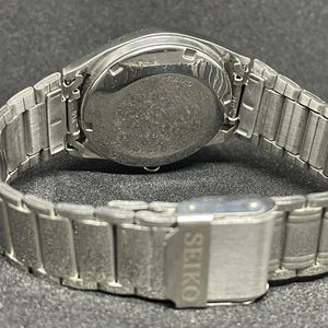 Pu&ograve; includere: Un orologio da polso Seiko argentato, visto dal retro, che mostra il cinturino e la chiusura. Il cinturino dell'orologio &egrave; composto da segmenti metallici. La chiusura riporta il marchio Seiko.