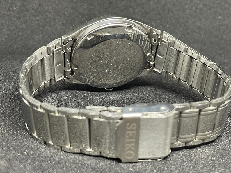 Pu&ograve; includere: Un orologio da polso Seiko argentato, visto dal retro, che mostra il cinturino e la chiusura. Il cinturino dell'orologio &egrave; composto da segmenti metallici. La chiusura riporta il marchio Seiko.