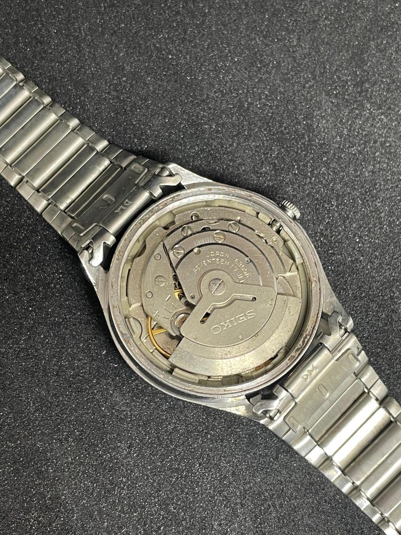 Pu&ograve; includere: Un orologio Seiko vintage con cinturino in metallo argentato. Il quadrante dell'orologio &egrave; aperto, rivelando gli intricati meccanismi interni. Il movimento dell'orologio &egrave; visibile, con la scritta "SEIKO".