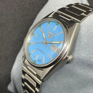 Pu&ograve; includere: Un orologio automatico Seiko 5 argentato con quadrante azzurro. L'orologio presenta un cinturino argentato e un display giorno-data. Il quadrante ha lancette e indici argentati. L'orologio &egrave; contrassegnato "AUTOMATIC" e "JAPAN MADE".