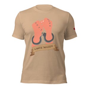 May include: Tan t-shirt featuring a graphic of two hands in handcuffs with tattoos. A banner below the hands reads "CARPE NOCTEM". The shirt has a crew neck and short sleeves.