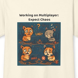 Op de afbeelding: Crèmekleurig T-shirt met een cartoonafbeelding van katten die gamen. De afbeelding bevat de tekst "Working on Multiplayer: Expect Chaos", evenals de woorden "LAG?" en "BUGS". De katten dragen een koptelefoon en tonen verschillende emoties.