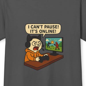 Op de afbeelding: Donkergrijs t-shirt met een cartoon kat gamer met een koptelefoon en een oranje hoodie, die een gamecontroller vasthoudt. De kat kijkt naar een computerscherm met een game scene. Tekst: "I CAN'T PAUSE! IT'S ONLINE!"