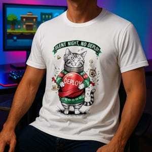 Könnte beinhalten: Weißes T-Shirt mit einer Cartoon-Katze, die ein Headset und einen Weihnachtspullover trägt und eine rote Kugel mit dem Wort "DEPLOY" hält. Das T-Shirt hat den Text "SILENT NIGHT, NO DEPLOY" über der Katze.