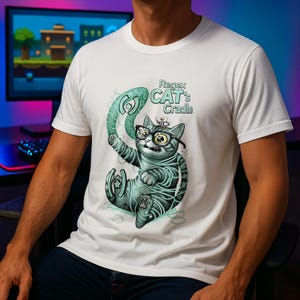 Può includere: T-shirt bianca con un disegno di un gatto dei cartoni animati con occhiali e avvolto in spago, con la scritta "Regex CAT's Cradle". Il gatto tiene in mano un oggetto verde curvo. Il design è in tonalità di grigio e verde acqua.
