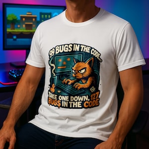 Könnte beinhalten: Weißes T-Shirt mit einer Cartoon-Katze, die an einem Computer arbeitet. Der Text lautet: "99 BUGS IN THE CODE... TAKE ONE DOWN, 127 BUGS IN THE CODE." Die Katze ist orange und hat einen wütenden Gesichtsausdruck. Eine Kaffeetasse und eine Ente sind ebenfalls zu sehen.