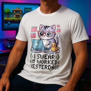 May include: White t-shirt with a cartoon cat wearing glasses and working on a laptop. The cat is next to a rubber duck, with the text "I SWEAR IT WORKED YESTERDAY!"