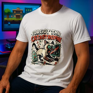 Könnte beinhalten: Weißes T-Shirt mit einem Cartoon-Katzendesign. Die Katze hat grüne Augen und rennt vor einem zerbrochenen Bildschirm davon. Der Text auf dem Shirt lautet "FORGOT THE CATASTROPHE". Das Design ist im Comic-Stil.