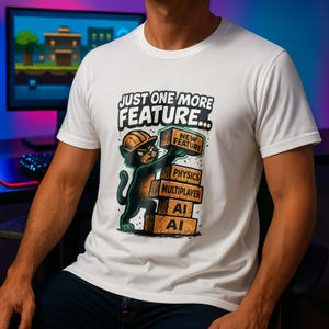 May include: White t-shirt with a cartoon cat in a construction hat, holding a brick saying "NEW FEATURE." Other bricks read "PHYSICS," "MULTIPLAYER," "AI," and "AI." The shirt has the text "JUST ONE MORE FEATURE..." above the cat.