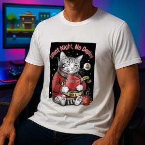 Könnte beinhalten: Weißes T-Shirt mit einer Cartoon-Katze, die ein Headset und einen roten Pullover trägt und einen roten Knopf mit der Aufschrift "DEPLOY" hält. Der Text "Silent Night, No Deploy" und "NOEL" sind ebenfalls abgebildet. Eine Tasse Kaffee mit Pfotenabdruck ist ebenfalls zu sehen.