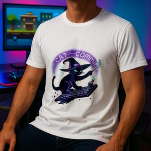 Puede incluir: Camiseta blanca con un gato negro con sombrero de bruja y varita mágica, con el texto "CAT COMMIT" en un círculo morado. El gato está sobre un teclado, con una botella de poción.