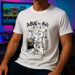 May include: White t-shirt with a cartoon cat decorating a computer monitor with bug-shaped Christmas lights. The text "DeBUG the Halls" is above the cat. The cat is white with a grey tail and is standing in front of a computer monitor.