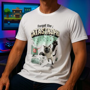 Op de afbeelding: Wit t-shirt met een cartoonafbeelding. Het toont een Siamees kat die uitreikt naar een computermonitor met het nummer nul. De tekst luidt "Forgot the; CATASTROPHE". Het ontwerp bevat een gebroken pot en groene accenten.