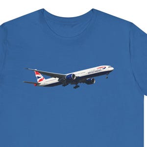 May include: Royal blue t-shirt with a graphic of a Boeing 777 aircraft in flight. The plane is white with red and blue details and the British Airways logo. The shirt is a solid colour.