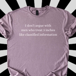 May include: A mauve-colored t-shirt with rolled-up sleeves. The shirt features the text: "I don't argue with men who treat 3 inches like classified information."
